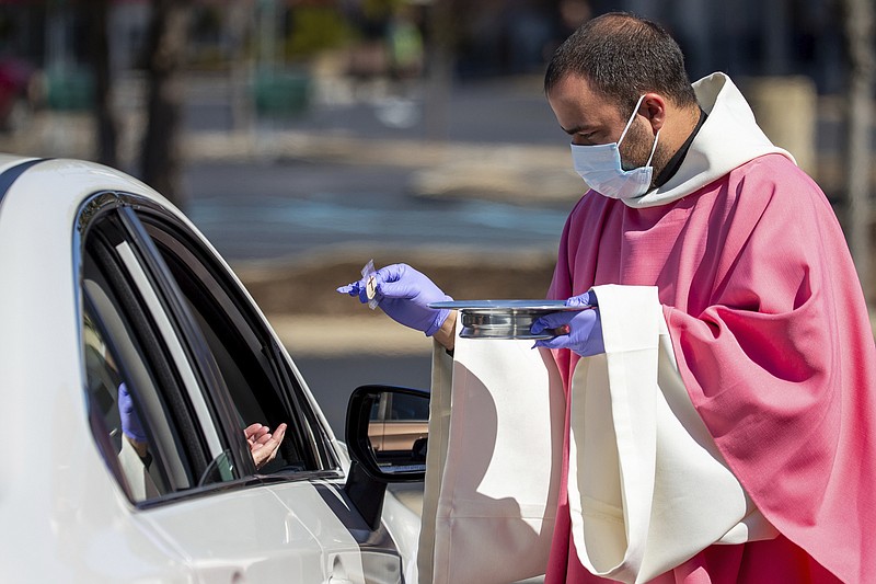 FILE - In this Sunday, March 22, 2020 file photo, the Rev. William A. Mentz, pastor of the Scranton, Pa.-based St. Francis and Clare Progressive Catholic Church, wears a mask and gloves while distributing prepackaged communion to the faithful attending Mass while sitting in their cars in the parking lot of a shopping center in Moosic, Pa. The Progressive Catholic Church is a small denomination operating independently of the Roman Catholic Church. Other Catholic churches in the Scranton area suspended the celebration of mass to help control the spread of COVID-19. (Christopher Dolan/The Times-Tribune via AP)
