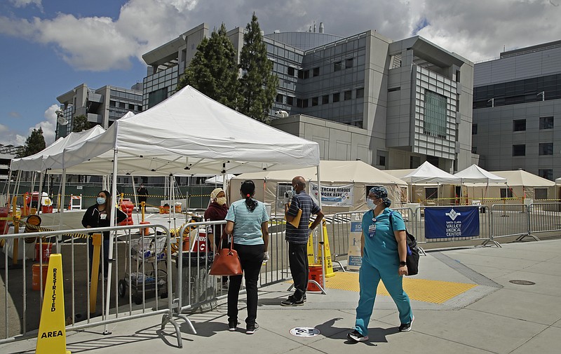 A healthcare worker walks past people waiting to be tested for COVID-19 on Tuesday, May 19, 2020, at Santa Clara Valley Medical Center in San Jose, Calif. Confirmed COVID-19 patients in Bay Area hospitals has dropped by more than half since the peak of 471 reported on April 7. (AP Photo/Ben Margot)