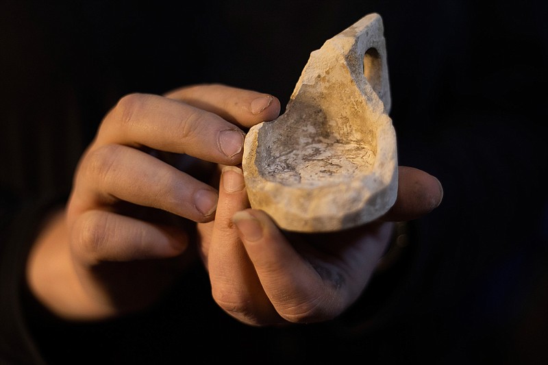 An Israel Antiquities Authority archaeologist holds a chalk measuring cup from early Roman period at an excavation site beneath the Western Wall, in Jerusalem's Old City, Tuesday, May 19, 2020. Israeli archaeologists excavating in Jerusalem exhibited a recently uncovered, unusual series of 2,000-year-old chambers carved out of the bedrock beneath the Western Wall plaza on Tuesday. The excavations are uncovering new sections of a sprawling network of ancient subterranean passageways running alongside a contested Jerusalem holy site known to Jews as the Temple Mount and to Muslims as the Noble Sanctuary. (AP Photo/Ariel Schalit)