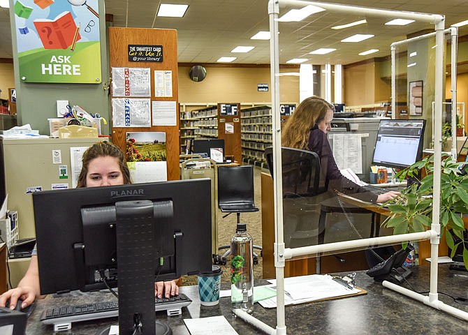 Teen Services Associate Megan Mehmert, left, works at her computer Tuesday while Courtney Waters, teen services coordinator for Missouri River Regional Library, answers a phone call. Plexiglass, fewer chairs around tables and other changes have been made as the staff of
MRRL prepares for next week's reopening.