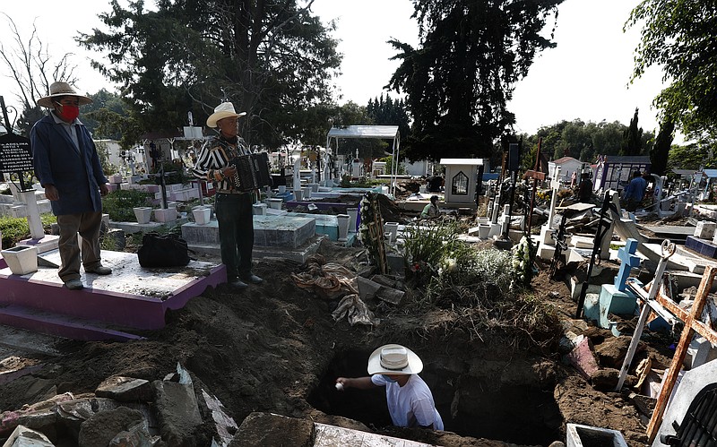 Cemetery musician Victor Dzib Cima, 70, plays his accordion as he waits for clients while cemetery workers remove coffins from gravesites that belonged to families who stopped paying rent at the San Nicolas Tolentino Pantheon, where he has worked for tips for 22 years, in the Iztapalapa area of Mexico City, Friday, May 22, 2020. The cemetery is making space for more burials amid the COVID-19 pandemic, and it is custom for cemeteries in Mexico to rent, instead of sell, grave sites. (AP Photo/Marco Ugarte)