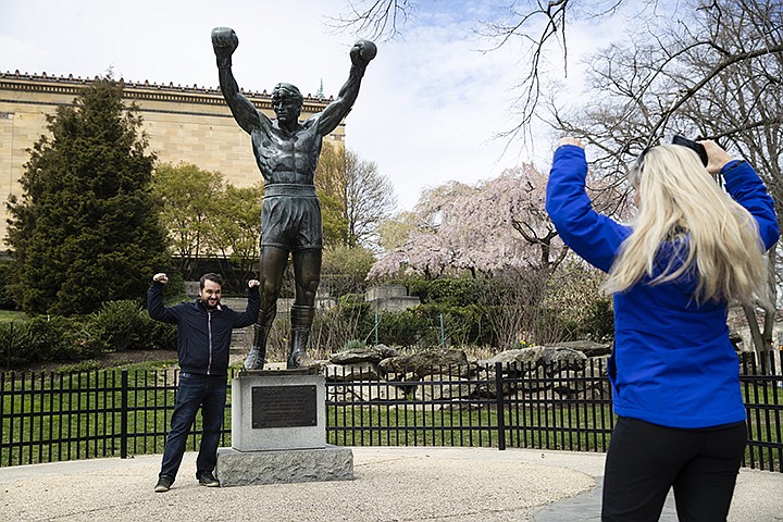 In this April 3, 2020, photo, Jessica Shiroff, right, directs exchange student Joao Martucci, of Brazil, as he poses for a photograph with the Rocky Statue at the Philadelphia Art Museum in Philadelphia. "Rocky" finished tied for No. 2 in The Associated Press Top 25 favorite sports movies poll. (AP Photo/Matt Rourke)