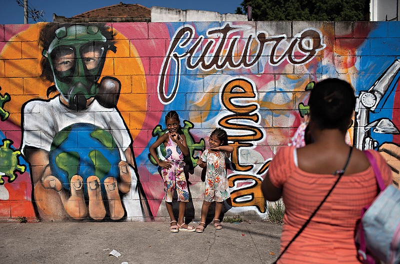 A woman takes photos of her daughters by a mural referencing the COVID-19 pandemic, painted in honor of health workers in Rio de Janeiro, Brazil. The mural is by graffiti artist Angelo Campos, 39, who has lost two relatives to the new coronavirus.