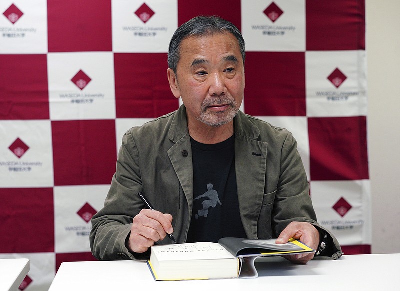 FILE - In this Nov. 3, 2018, file photo, Japanese novelist Haruki Murakami signs his autograph on his novel "Killing Commendatore" during a press conference at Waseda University in Tokyo. The acclaimed Japanese novelist Murakami, hosting a special radio show from home, painted a brighter side of the world with his favorite music, and said Friday, May 22, 2020, the fight against the coronavirus is a challenge to human wisdom in figuring out ways to help and care each other. (AP Photo/Eugene Hoshiko, File)