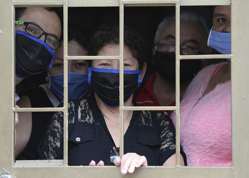 A family peers from the window of their home as they wait to receive boxes of free food, during a lockdown to curb the spread of the new coronavirus, in Bogota, Colombia, Monday, May 4, 2020. The U.N. World Food Program is warning that upward of at least 14 million people could go hungry in Latin America as the coronavirus pandemic rages on, shuttering people in their homes, drying up work and crippling the economy. (AP Photo/Fernando Vergara)