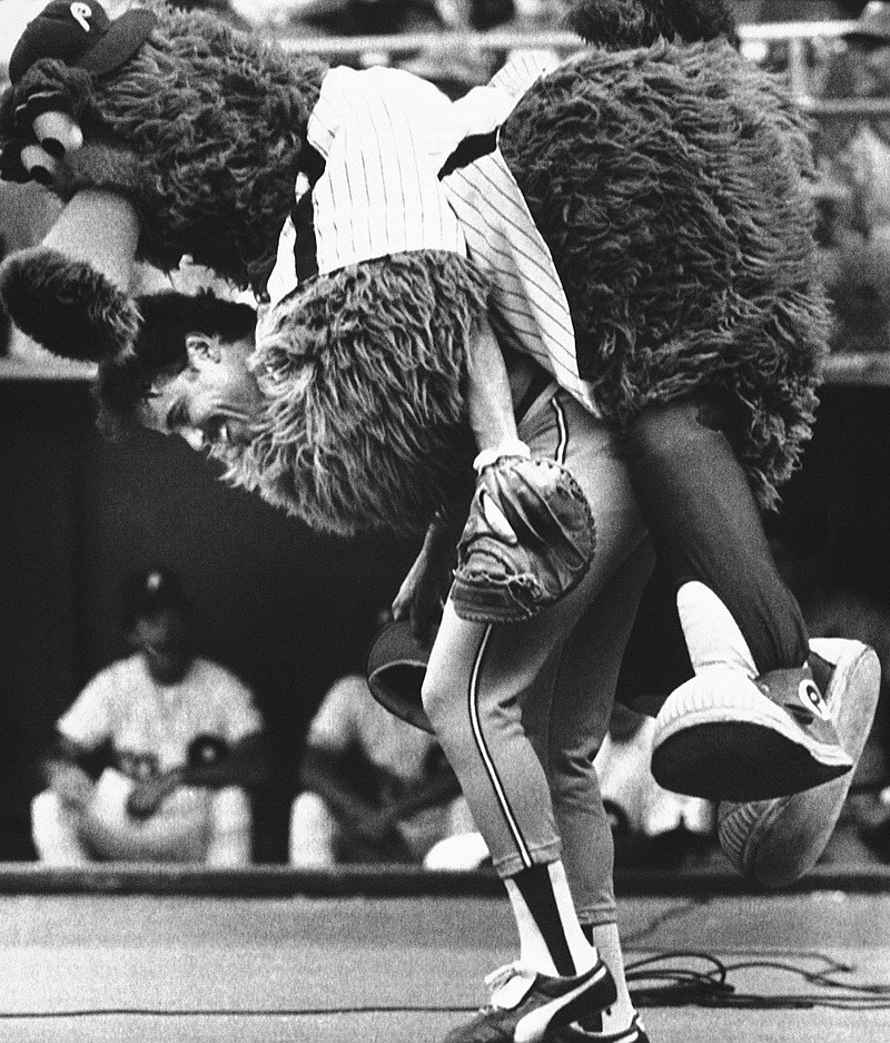 In this July 12, 1983, file photo, the Phillie Phanatic jumps onto the back of Atlanta Braves catcher Biff Pocoroba, who didn't see the Phillies mascot coming a warmup before a baseball doubleheader in Philadelphia. Pocoroba, who played in the 1978 All-Star Game and was a backup on the Braves team that won an improbable NL West title in 1982, has died at age 66. (AP Photo/Rusty Kennedy, File)