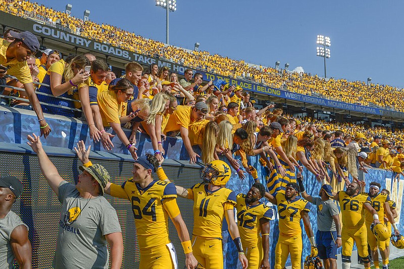 In this Oct. 6, 2018, file photo, West Virginia players high-five fans after defeating Kansas 38-22 in an NCAA college football game in Morgantown, W. Va. The crippling coronavirus pandemic has brought the entire world — including the sports world — to a standstill, and it shows no sign of going away anytime soon. That has left fans, stadium workers, team owners, sponsors and yes, even players, wondering what life will be like when games finally resume. (AP Photo/Craig Hudson, File)