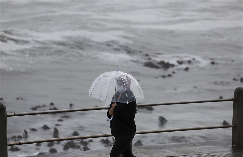 A woman walks on the promenade in stormy weather in Sea Point, Cape Town, South Africa, Friday, May 29, 2020. With dramatically increased community transmissions, Cape Town has become the center of the coronavirus outbreak in South Africa. (AP Photo/Nardus Engelbrecht)