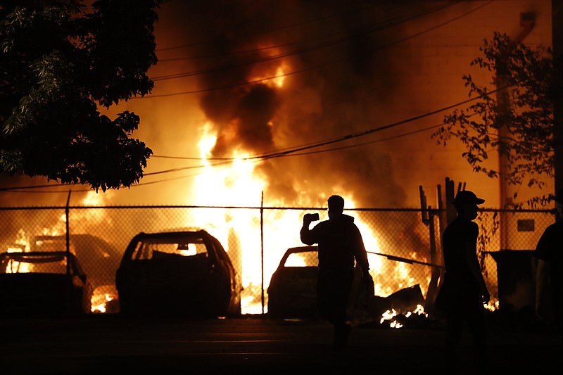 People watch a fire Friday, May 29, 2020, in Minneapolis. Protests continued following the death of George Floyd who died after being restrained by Minneapolis police officers on Memorial Day. (AP Photo/Julio Cortez)