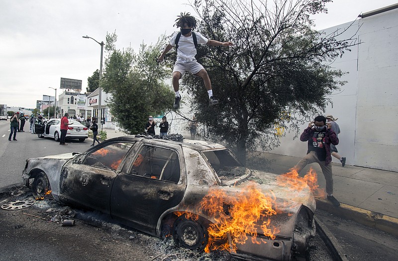 A person jumps on a burning police vehicle in Los Angeles, Saturday, May 30, 2020, during a protest over the death of George Floyd. Floyd died in Minneapolis police custody on Memorial Day. (AP Photo/Ringo H.W. Chiu)