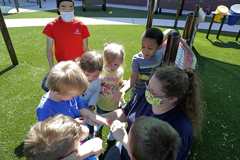 In this May 27, 2020 photo, teachers Jana Blair, right, and Aaron Rainboth, upper left, wear masks as they work with kids examining a spider they found on the playground at the Frederickson KinderCare daycare center, in Tacoma, Wash. In a world weary of the coronavirus, many working parents with young children are now struggling with the decision on when or how they'll be comfortable returning to their child care providers. Frederickson KinderCare has been open throughout the pandemic to care for children of essential workers. (AP Photo/Ted S. Warren)