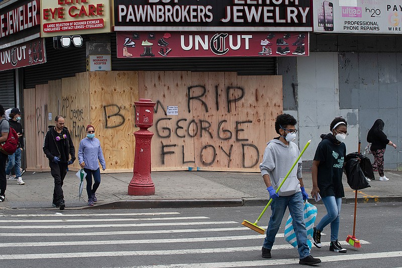 Volunteers Christian Tyler and Ashante West, right, carry brooms after participating in a community cleanup effort as they walk by a boarded up pawnbroker's store, Tuesday, June 2, 2020, in the Fordham Road area of the Bronx borough of New York. Protesters broke into stores Monday night in reaction to George Floyd's death while in police custody on May 25 in Minneapolis. (AP Photo/Mark Lennihan)