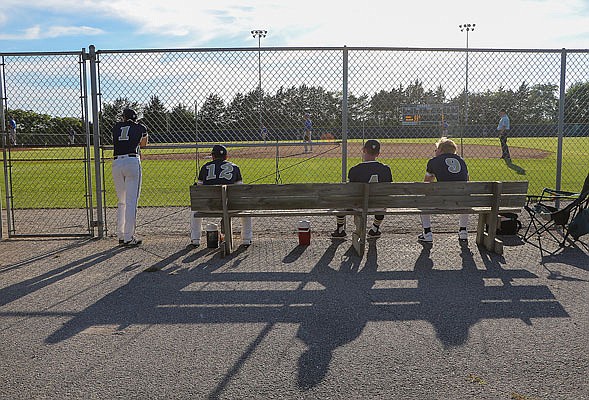 Helias players sit on a bench outside the dugout during the first game of Tuesday night's doubleheader against Fatima at the American Legion Post 5 Sports Complex. The bench served as extra space for players to sit in order to maintain social distancing guidelines.