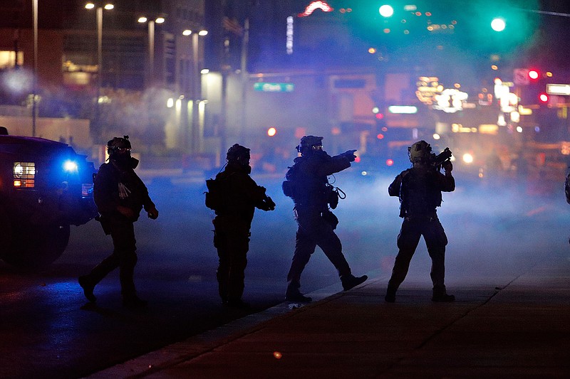 In this May 30, 2020, file photo, police walk through tear gas as they try to disperse protesters in Las Vegas. Three Nevada men with ties to a loose movement of right-wing extremists advocating the overthrow of the U.S. government have been arrested on terror charges in what authorities say was a conspiracy to spark violence during recent protests in Las Vegas. (AP Photo/John Locher, File)