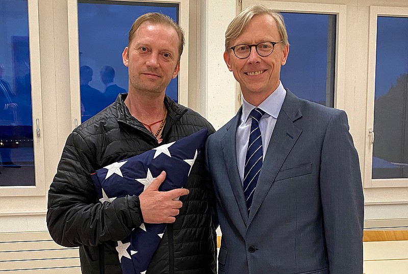 In this image provided by the U.S. State Department, Michael White holds an American flag as he poses for a photo Thursday, June 4, 2020, with U.S. special envoy for Iran Brian Hook at the Zurich, Switzerland, airport after White's release from Iran.  White, a Navy veteran who's been detained in Iran for nearly two years has been released and is making his way home, with the first leg on a Swiss government aircraft. (U.S. State Department via AP)