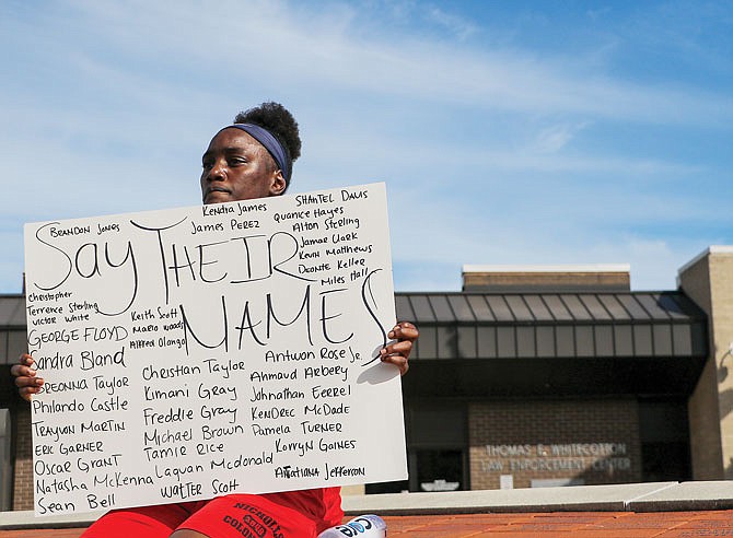 Brenisha Coleman sits Friday in front of the Jefferson City Police Department with a sign that she made, listing the names of black people who died in police custody or killed by police, ex-police or armed white people in recent years. She said she tried to fill in as many as she could, but she ran out of room. 