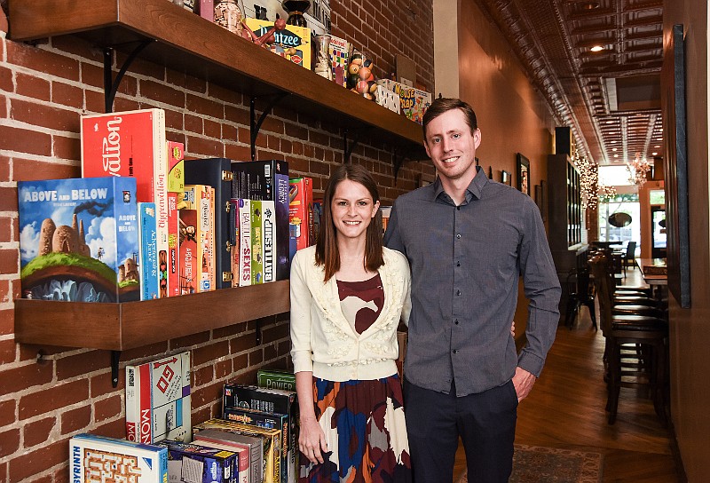 Cara and Adam Stark, owners of downtown Jefferson City's Cork and Board, pose near the couple's more than 100 board games from which customers can choose to play while enjoying wine, beer or mixed drinks.
