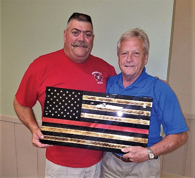 Bill Farr, right, holds a handcrafted flag made by Darren Reuter that honors his decades of service as a firefighter. Farr's extensive public service career began in 1969 when he volunteered for the draft with the U.S. Army.