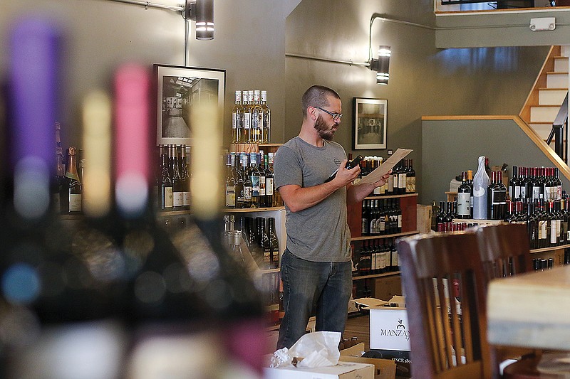 Will Beever works on pricing and organizing bottles of wine Tuesday on the floor of Barvino. As of right now, there are two tables open for visitors to sit outside. The tables and chairs that were once on the main floor of the bar have migrated upstairs to make room for selling bottles of wine and spirits to takeout customers. 