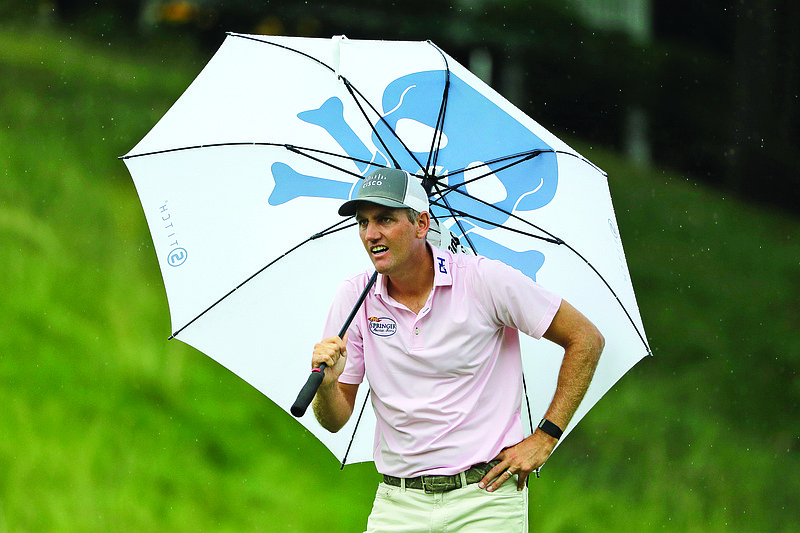 Brendon Todd looks at a competitor's tee shot while sheltering from the rain with an umbrella on the 18th hole during Saturday's third round of the Travelers Championship at TPC River Highlands in Cromwell, Conn.