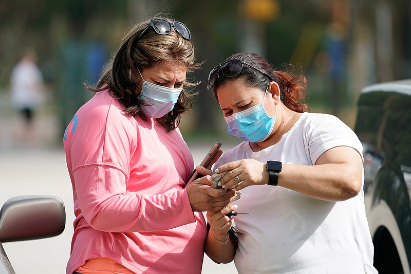 Women wear masks as they check a mobile phone Wednesday, July 1, 2014, in Houston. Harris County Commissioners have voted to extend the recently-issued mask order until August 26. The order directs any businesses providing goods or services to require all employees and visitors to wear face coverings in areas of close proximity to co-workers or the public. (AP Photo/David J. Phillip)