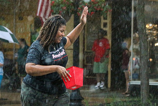 Despite the rainfall, Alicia Edwards with Building Community Bridges, waves to passerby during the Red, White and Bloom Parade on High Street Friday evening. 