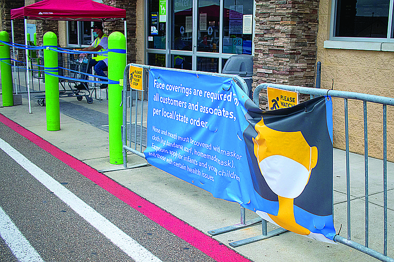 A sign requiring shoppers to wear a mask sits at the entrance of Walmart Neighborhood Market on Richmond Road. A worker sits next to the door monitoring how many customers are in the store. 