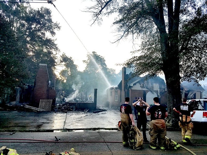 As Texarkana, Texas, firefighters look on, water streams from an elevated hose onto the remains of a house that burned early Tuesday morning in the 2000 block of Olive Street. All eight residents, including six children, escaped unharmed. The house next door caught fire first, around 3:30 a.m., and that fire claimed the life of an elderly man. (Staff photo by Karl Richter)