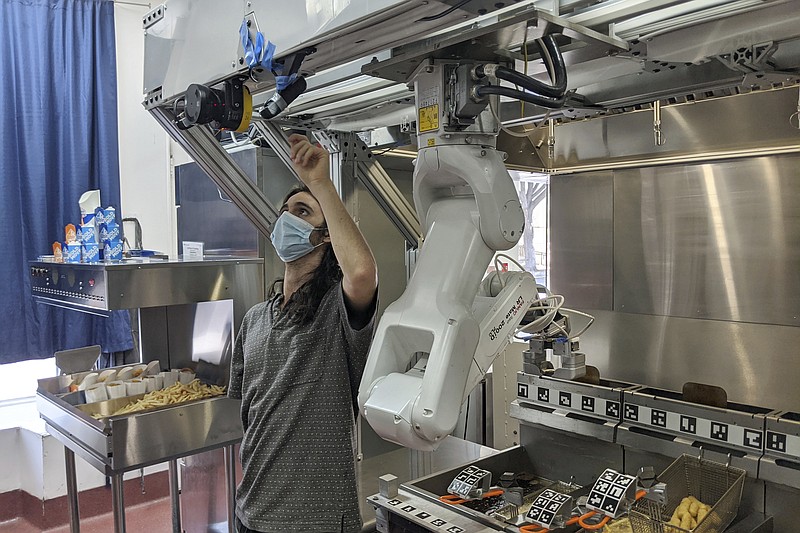 A technician makes an adjustment to a robot at Miso Robotics' White Castle test kitchen in Pasadena, Calif., Thursday, July 9, 2020. Robots that can flip burgers, make salads and even bake bread are in growing demand as virus-wary kitchens try to put some distance between workers and customers. Starting this fall, the White Castle burger chain will test the robot arm that can cook french fries and other foods.  The robot, dubbed Flippy, is made by Pasadena, California-based Miso Robotics.  (Miso Robotics via AP)
