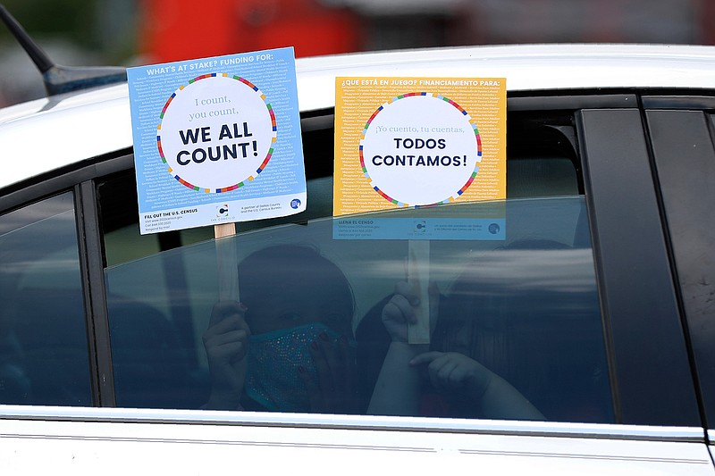 Two young children hold signs through the car window that make reference to the 2020 U.S. Census on June 25 as they wait in the car with their family at an outreach event in Dallas