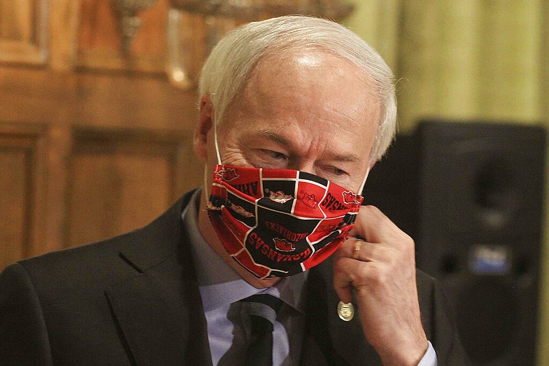 In this April 27, 2020 file photo, Gov. Asa Hutchinson takes off his Arkansas Razorbacks facemark as he arrives for the daily coronavirus briefing at the state Capitol in Little Rock.