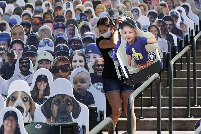 Seattle Mariners worker Lindsay Garza carries cutouts of fans to place in seats at the team's ballpark as part of the "Mariners Seat Fleet", Monday, July 27, 2020, in Seattle. The Mariners open play at home against the Oakland Athletics on Friday. For $30, fans can buy a version of themselves that will sit in at all home games. A portion of every purchase will be donated to non-profit organizations supporting COVID-19-related relief efforts. If a cutout "catches" a foul ball during a game, the team will mail the fan the baseball. (AP Photo/Elaine Thompson)