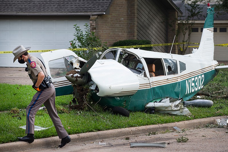 A law enforcement officer works at the site of the crash of a plane, in the front yard of a home Tuesday, July 28, 2020 in Houston. Two people were injured when a single-engine airplane crashed in a residential area early Tuesday, authorities said. The airplane hit a tree and landed in a front yard shortly before 2 a.m. (Brett Coomer/Houston Chronicle via AP)