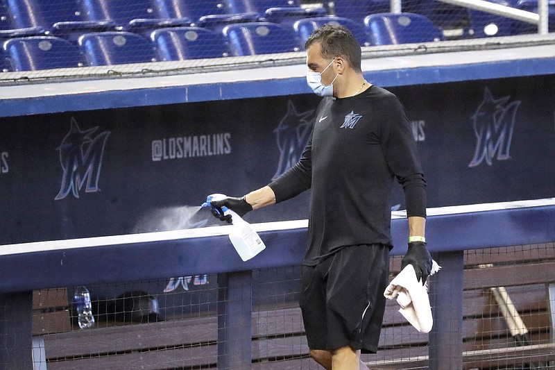 In this July 16 file photo, a worker sprays the dugout rail to help prevent the spread of the coronavirus before the Marlins' practice at Marlins Park in Miami.