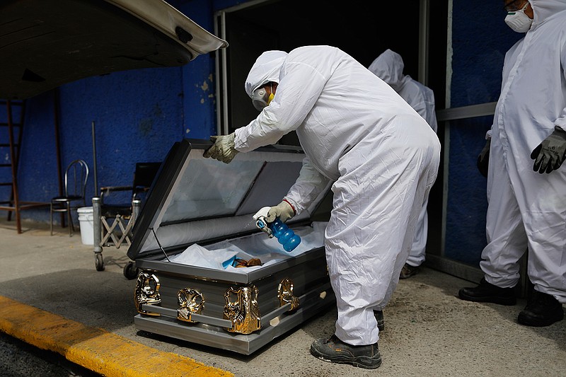 A worker wearing protective gear sprays disinfectant solution inside the coffin of a person who died from suspected COVID-19, as the body arrives at the crematorium at Xilotepec Cemetery in Xochimilco, Mexico City, Monday, July 27, 2020. (AP Photo/Rebecca Blackwell)