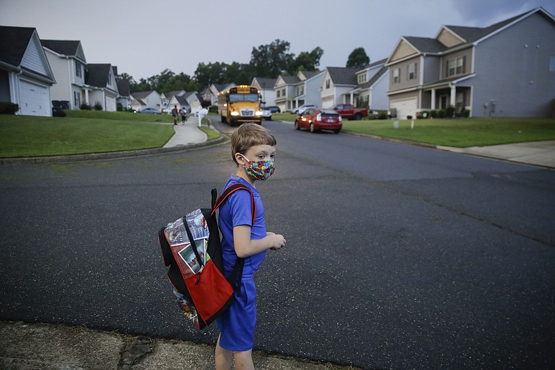 CORRECTS LAST NAME TO ADAMUS, NOT ADAMS - Paul Adamus, 7, waits at the bus stop for the first day of school on Monday, Aug. 3, 2020, in Dallas, Ga. Neighboring states arrived at differing conclusions on who’s in charge of the reopening of schools. The differences in philosophy underscore some of the difficulties facing states as they grapple with how to proceed amid growing coronavirus infections in numerous states. (AP Photo/Brynn Anderson)