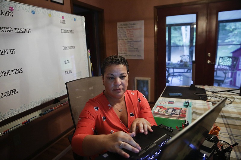 Aimee Rodriguez Webb works on her computer reading emails at her dinning room table that she set up as a virtual classroom for a Cobb County school, on Tuesday, July 28, 2020, in Marietta, Ga. After a rocky transition to distance learning last spring, Webb is determined to do better this fall. She bought a dry-erase board and a special camera to display worksheets, and she set up her dining room to broadcast school lessons. (AP Photo/Brynn Anderson)