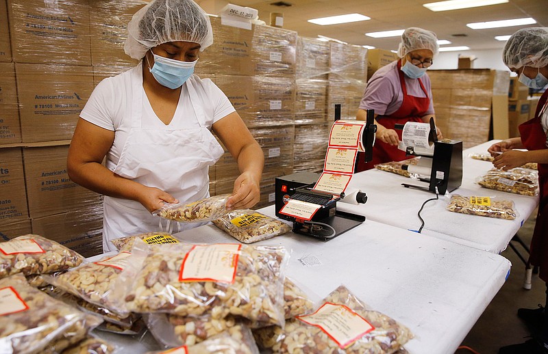Rebecca Gonzales works on applying new stickers on bags of mixed nuts previously planned for Hawaiian flight service at GNS Foods in Arlington, Texas, Tuesday, July 28, 2020. GNS Foods is working on selling bags of nuts to customers through its retail store. Sales to airlines has dropped dramatically due to the stoppage of serving nuts during the COVID-19 pandemic. (Vernon Bryant/The Dallas Morning News via AP)