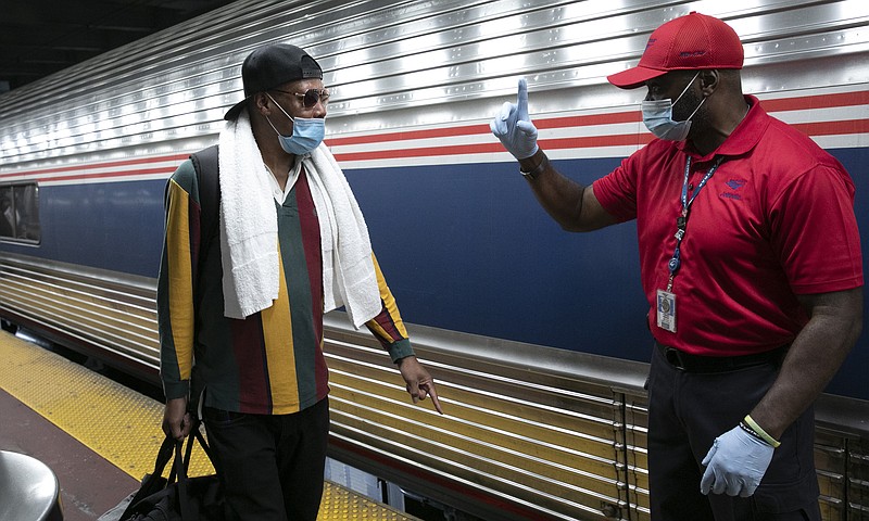 A traveler arriving on a train that originated in Miami gets directions from a porter, right, at Amtrak's Penn Station, Thursday, Aug. 6, 2020, in New York. Mayor Bill de Blasio is asking travelers from 34 states, including Florida where COVID-19 infection rates are high, to quarantine for 14 days after arriving in the city. (AP Photo/Mark Lennihan)