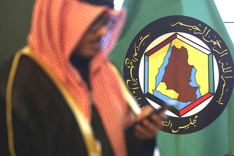 FILE - In this Dec. 5, 2017 file photo, a man looks at his mobile phone in front of the flag of the Gulf Cooperation Council, GCC, in Kuwait City. The GCC, a six-nation bloc of Gulf Arab nations torn apart by internal strife, unanimously endorsed on Sunday, Aug. 9, 2020, an extension of a United Nations arms embargo on Iran, just two months before it is set to expire. (AP Photo/Jon Gambrell, File)