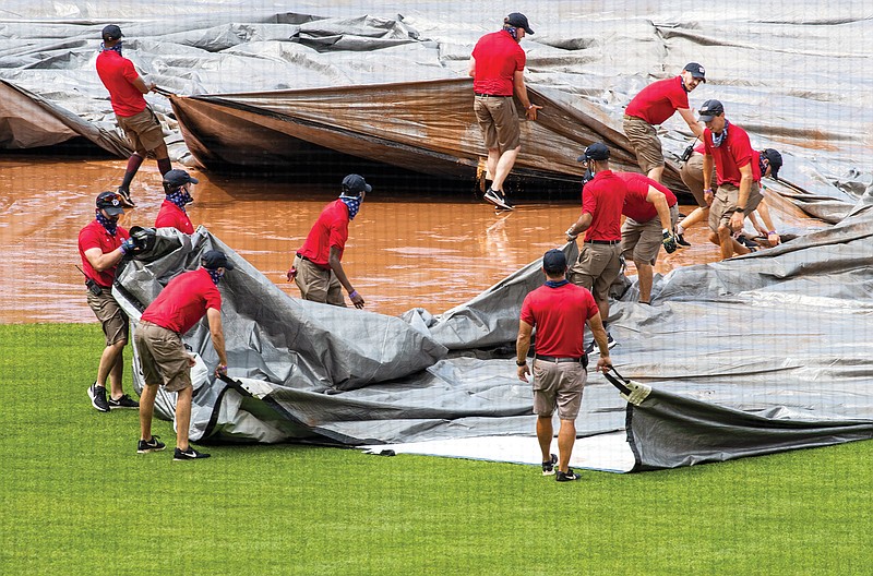 The grounds crew tries to untangle the tarp as they attempt to cover the infield from a heavy downpour delaying Sunday afternoon's game between the Nationals and the Orioles in Washington.
