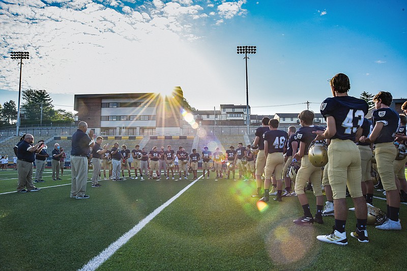 The morning sun rises Monday above the press box at Ray Hentges Stadium as football coach Chris Hentges addresses the Crusaders on the first official day of practice for the fall season.