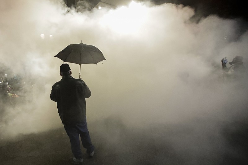 FILE - In this July 25, 2020, file photo, a protester carries an umbrella as federal police officers deploy tear gas during a protest at the Mark O. Hatfield U.S. Courthouse in Portland, Ore. Federal agents have left Portland, but city officials are still learning about and cleaning tear gas residue that lingers in the streets, dirt and possibly storm drains that empty into the Willamette River. (AP Photo/Marcio Jose Sanchez, File)