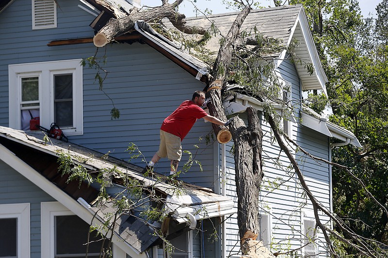 Mike Jacobis pushes a portion of tree trunk away as a neighbor helps on the ground in northwest Cedar Rapids, Iowa, on Wednesday, Aug. 12, 2020. The tree, which fell in Monday's storm, fell and damaged Jacobis' porch and the roof over a second-floor bedroom and closet. (Liz Martin/The Gazette via AP)