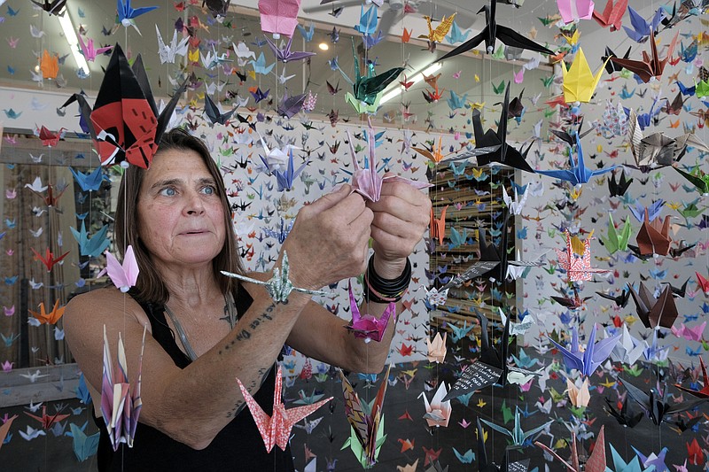 Artist Karla Funderburk, owner of Matter Studio Gallery, adjusts one of of the thousands of origami cranes hanging during an exhibit honoring the victims of COVID-19, Tuesday, Aug. 11, 2020, in Los Angeles. Funderburk started making the cranes three months earlier, stringing the paper swans in pink, blue, yellow and many other colors together and hanging them in her gallery.  (AP Photo/Richard Vogel)