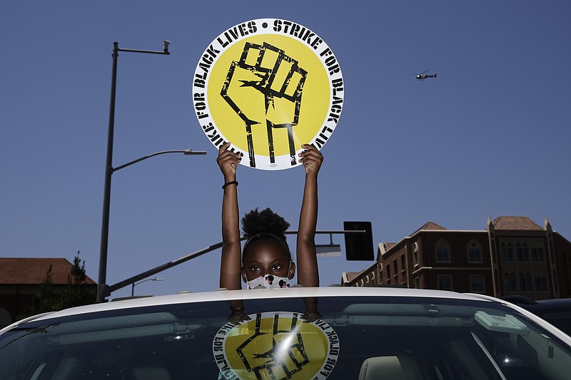 FILE - In this July 20, 2020, file photo, Audrey Reed, 8, holds up a sing through the sunroof of a car during a rally in Los Angeles. Ahead of Labor Day, major U.S. labor unions say they are considering work stoppages in support of the Black Lives Matter movement. (AP Photo/Jae C. Hong, File)