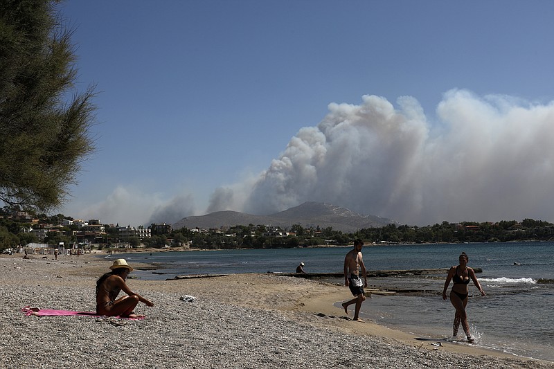 Flames burn behind the mountain as people walk next to the sea during a wildfire in Kalyvia, southeast of Athens, on Wednesday, Sept. 9, 2020. Greek firefighters, backed by water-dropping aircraft, were battling a string of wildfires near Athens and in other parts of the country Wednesday with efforts hampered by strong winds that whipped on the flames. (AP Photo/Yorgos Karahalis)