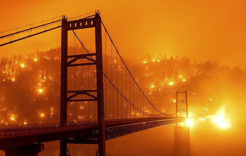 In this image taken with a slow shutter speed, embers light up a hillside behind the Bidwell Bar Bridge as the Bear Fire burns in Oroville, Calif., on Wednesday, Sept. 9, 2020. The blaze, part of the lightning-sparked North Complex, expanded at a critical rate of spread as winds buffeted the region. (AP Photo/Noah Berger)