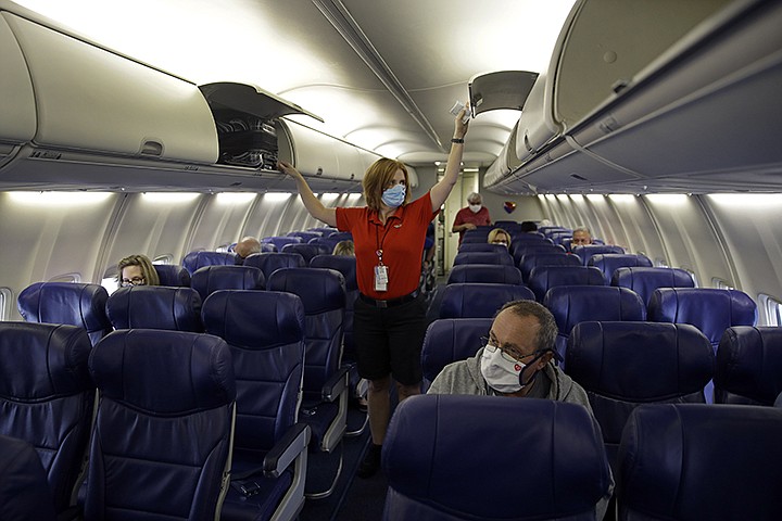 In this May 24, 2020 file photo, a Southwest Airlines flight attendant prepares a plane bound for Orlando, Fla. for takeoff at Kansas City International airport in Kansas City, Mo. Airline workers are making a last-ditch push for $25 billion in federal money to avoid furloughs for six more months. But critics including some lawmakers say the airlines need to shrink because fewer people are traveling.  (AP Photo/Charlie Riedel, File)
