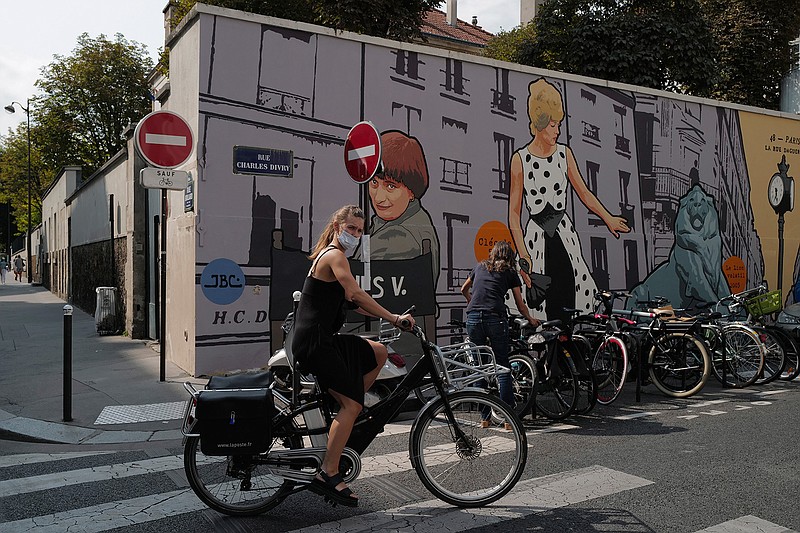 A woman, wearing a protective face mask as a precaution against the coronavirus, rides her bicycle front of a mural representing late film director Agnes Varda, in Paris, Friday, Sept. 11, 2020. French health authorities have reported on Thursday 9,843 infections from the coronavirus in 24 hours, the highest daily tally since the end of France's lockdown in April. France has seen a sharp uptick in new cases in recent weeks and hospitalizations have started to increase steadily, reaching now over 5,000 including 615 people in ICU. (AP Photo/Francois Mori)